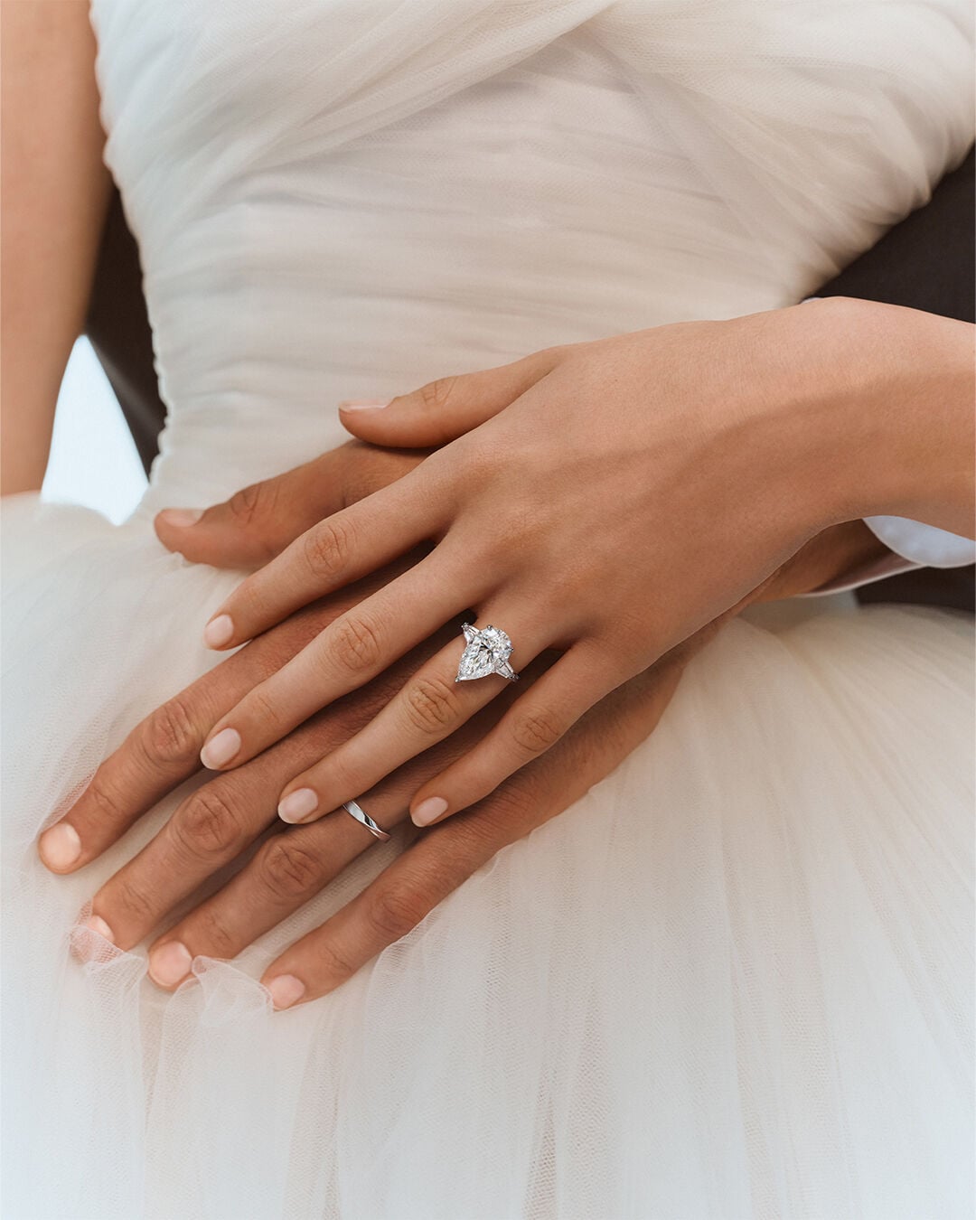Image shows model hands wearing Graff Pear Shape Promise engagement ring and Spiral wedding band 