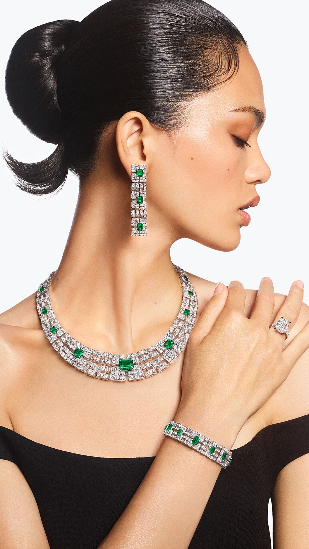 Image shows model wearing Graff white diamond and emerald jewellery suite 